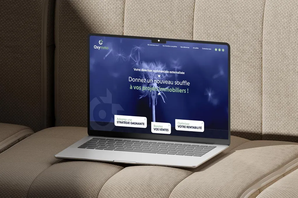 Page d'accueil du site internet d'Oxymmo sur un ordinateur, affichant le logo de l'agence, le menu et des visuels de projets immobiliers. Réalisation Prospectiv* Colmar